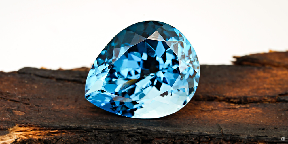 Loose Cut Blue Topaz Resting On Wood Bark Against White Background