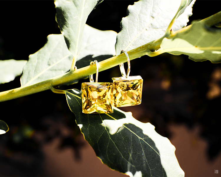 Restored Fine Jewelry Topaz Gemstone Earrings Hanging on Green Plant Branch Against Dark Background