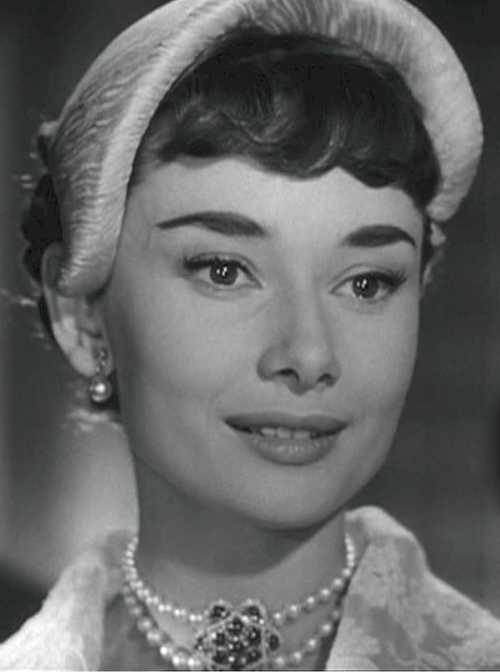 Black and White photo showcasing 1950s actress Audrey Hepburn wearing matching pearl necklace and earring set in her film, "Roman Holiday" circa 1953