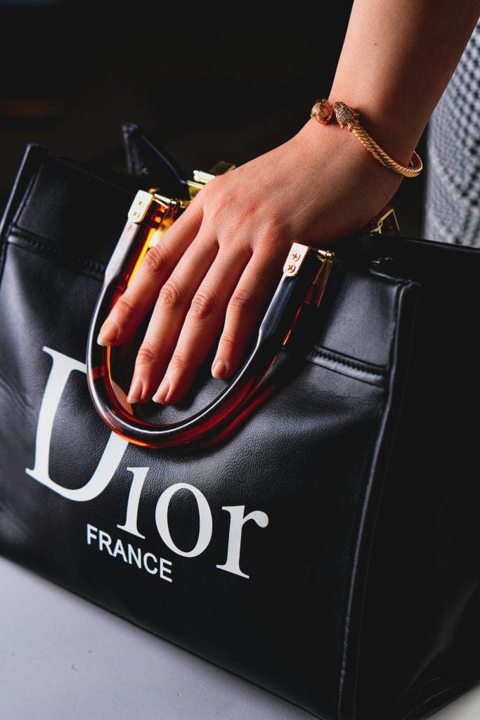 Image showcasing Dior bag with hand holding it wearing a Dior bracelet